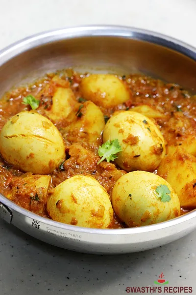A pan of aloo anday with potato chunks and golden boiled eggs in red tomato gravy, garnished with green chillies and coriander