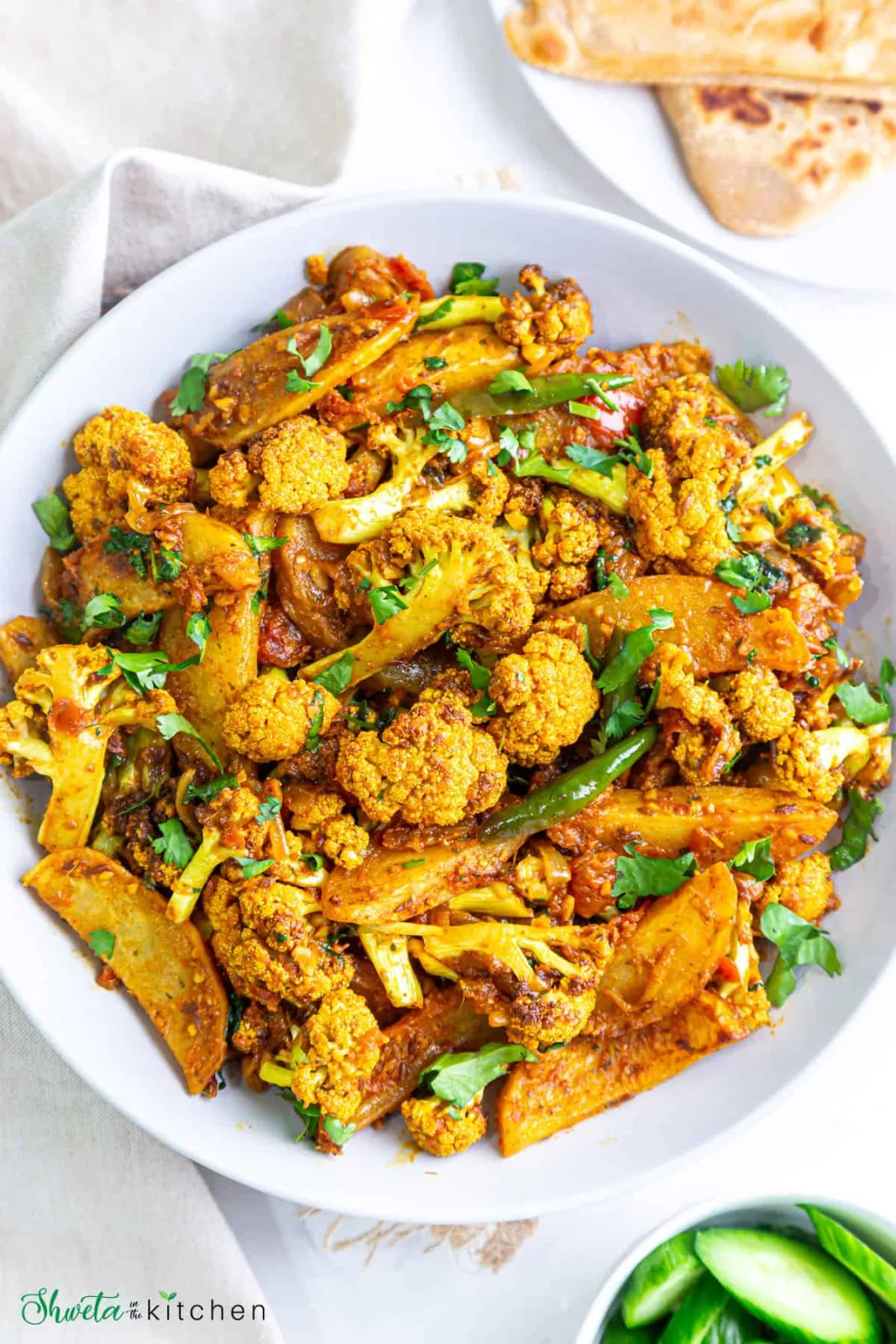 A karahi of dry-style aloo gobi with potato and cauliflower in golden masala, topped with ginger and coriander