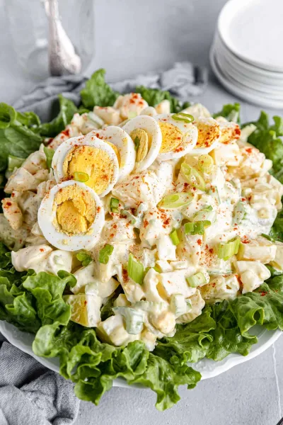 Bowl of creamy American potato salad topped with egg slices, paprika and parsley
