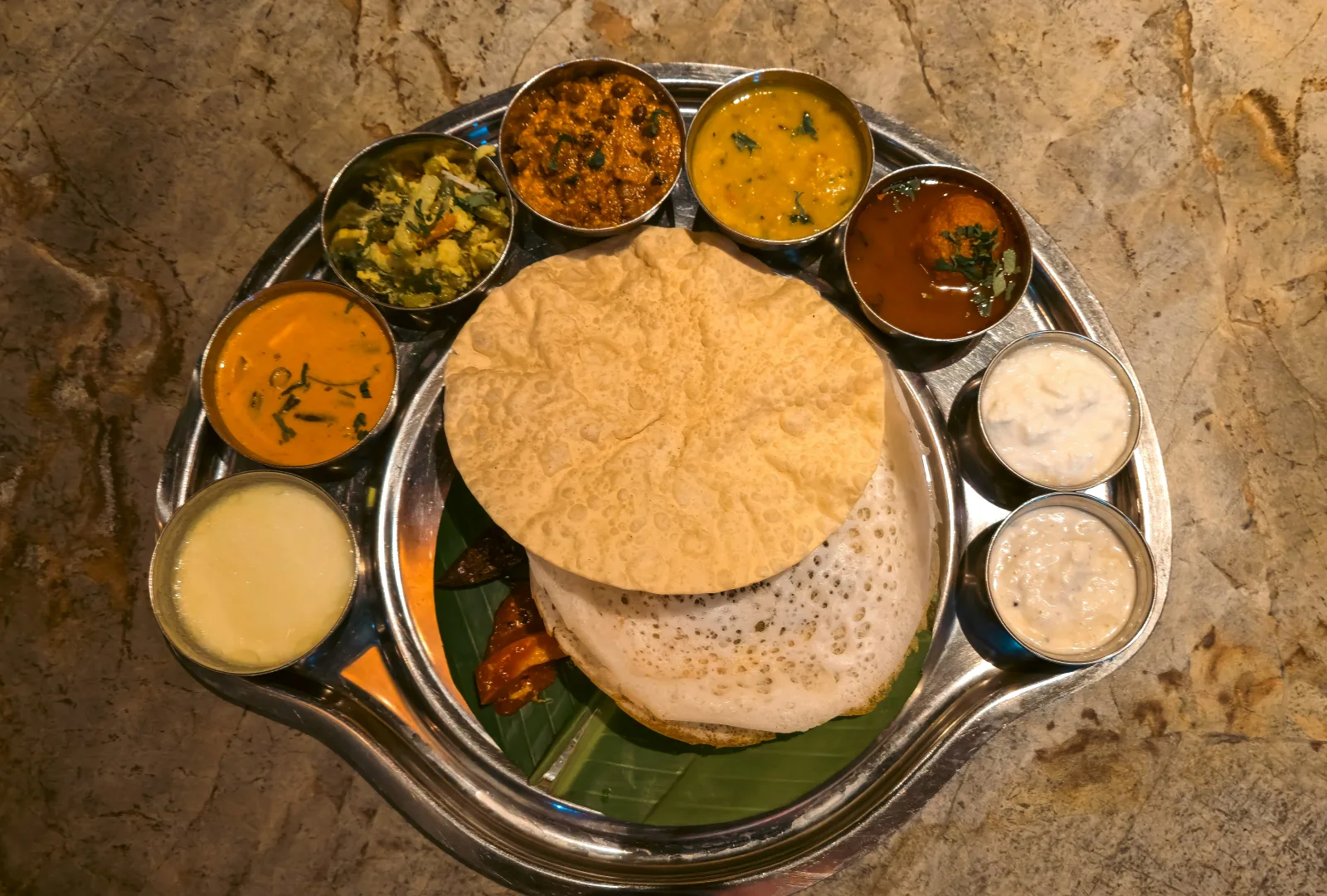 Golden lacy appams with fluffy white centres served with vegetable stew on a banana leaf