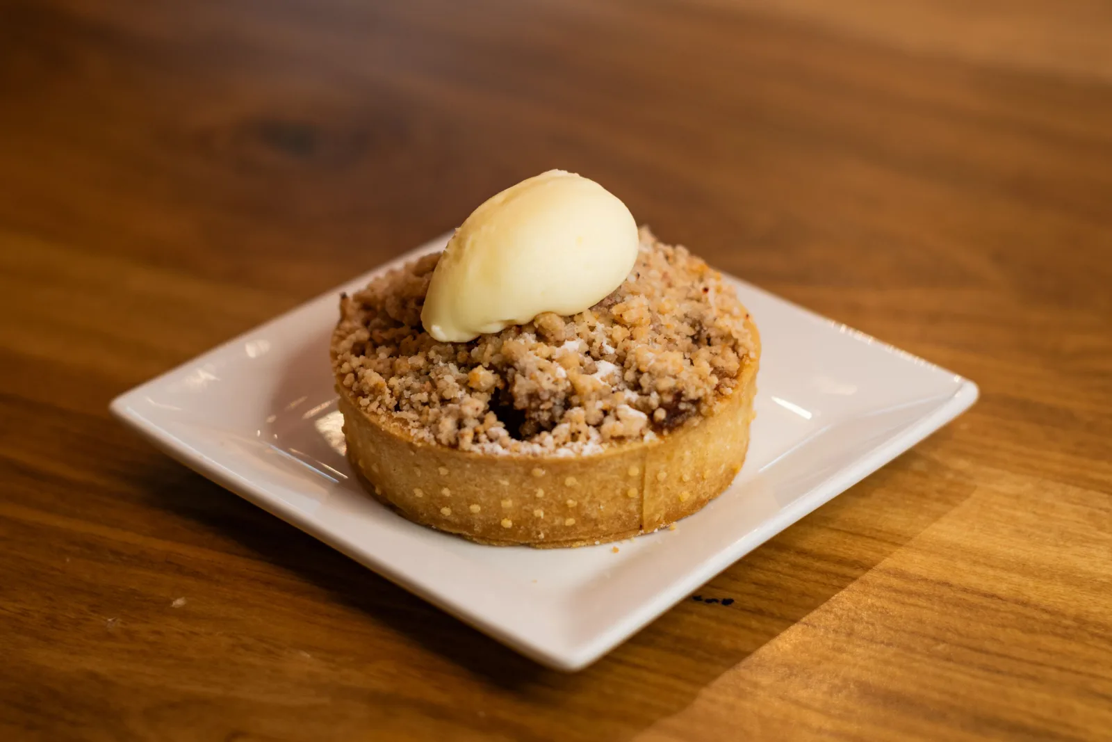 Golden apple crumble in a baking dish with a spoonful removed and a jug of custard beside it