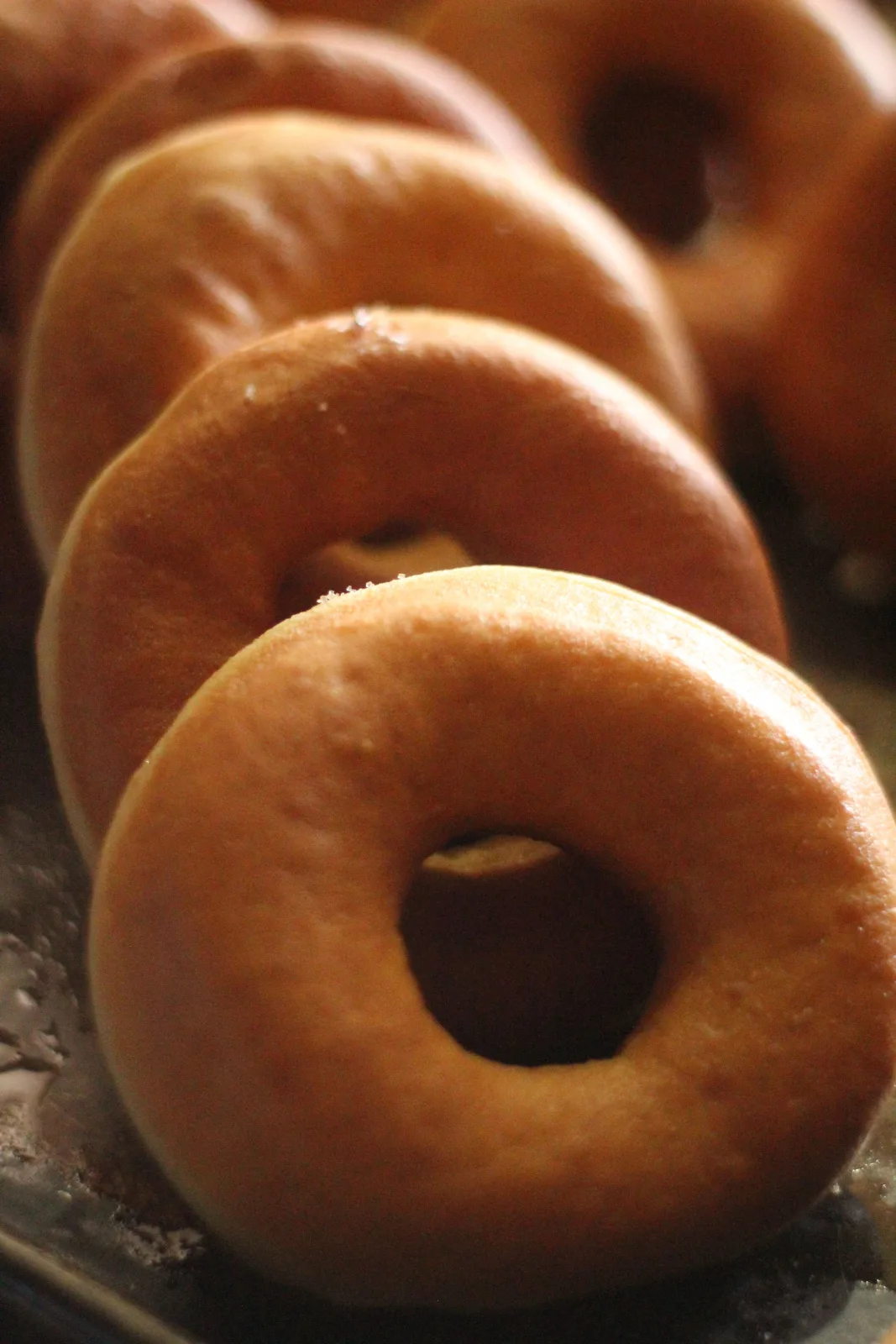Glazed baked doughnuts with sprinkles cooling on a wire rack beside a cup of tea