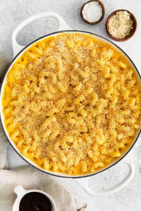 Golden baked macaroni and cheese in a baking dish with a crisp breadcrumb topping and a creamy spoonful lifted out