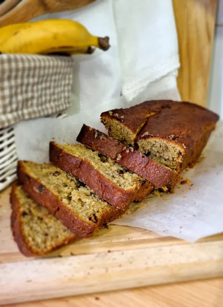 Sliced golden banana bread loaf with walnuts and butter on a wooden board