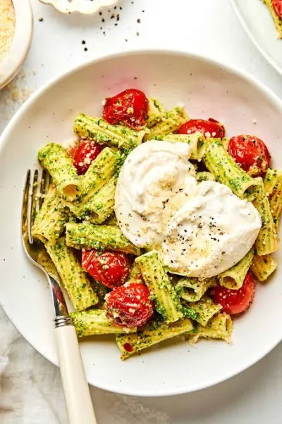 Bowl of spaghetti tossed in green basil pesto with blistered cherry tomatoes and grated Parmesan