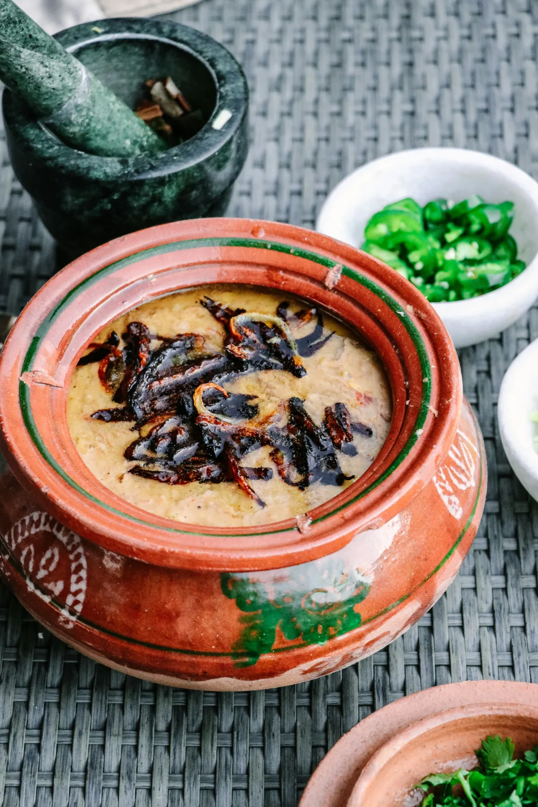 Bowl of beef haleem topped with fried onions, ginger, green chillies, fresh herbs and a lemon wedge