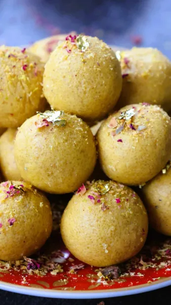 Golden besan ladoos topped with pistachio slivers on a brass plate