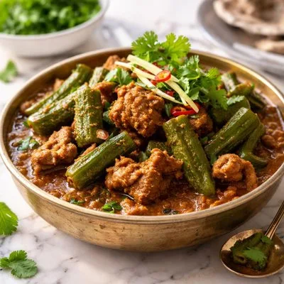 A pot of bhindi gosht with mutton pieces and green okra in a thick red-brown gravy, served with roti