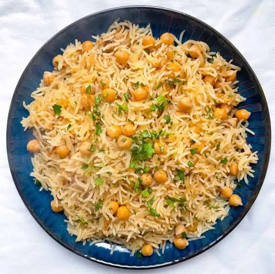A dish of chana pulao with basmati rice, chickpeas, fried onions and fresh herbs, served with raita and lemon.