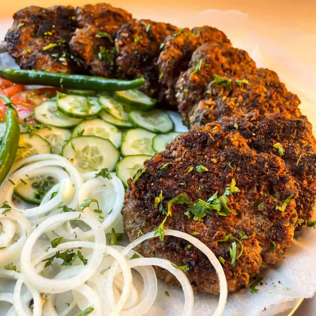 Golden brown chapli kababs on a slate board with naan, onion rings, lemon wedges and green chutney