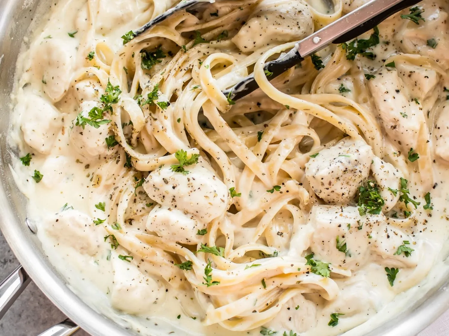 A bowl of fettuccine Alfredo topped with sliced seared chicken, parsley and grated Parmesan