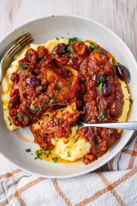Skillet of chicken cacciatore with browned chicken pieces in tomato sauce with peppers, mushrooms, olives and parsley
