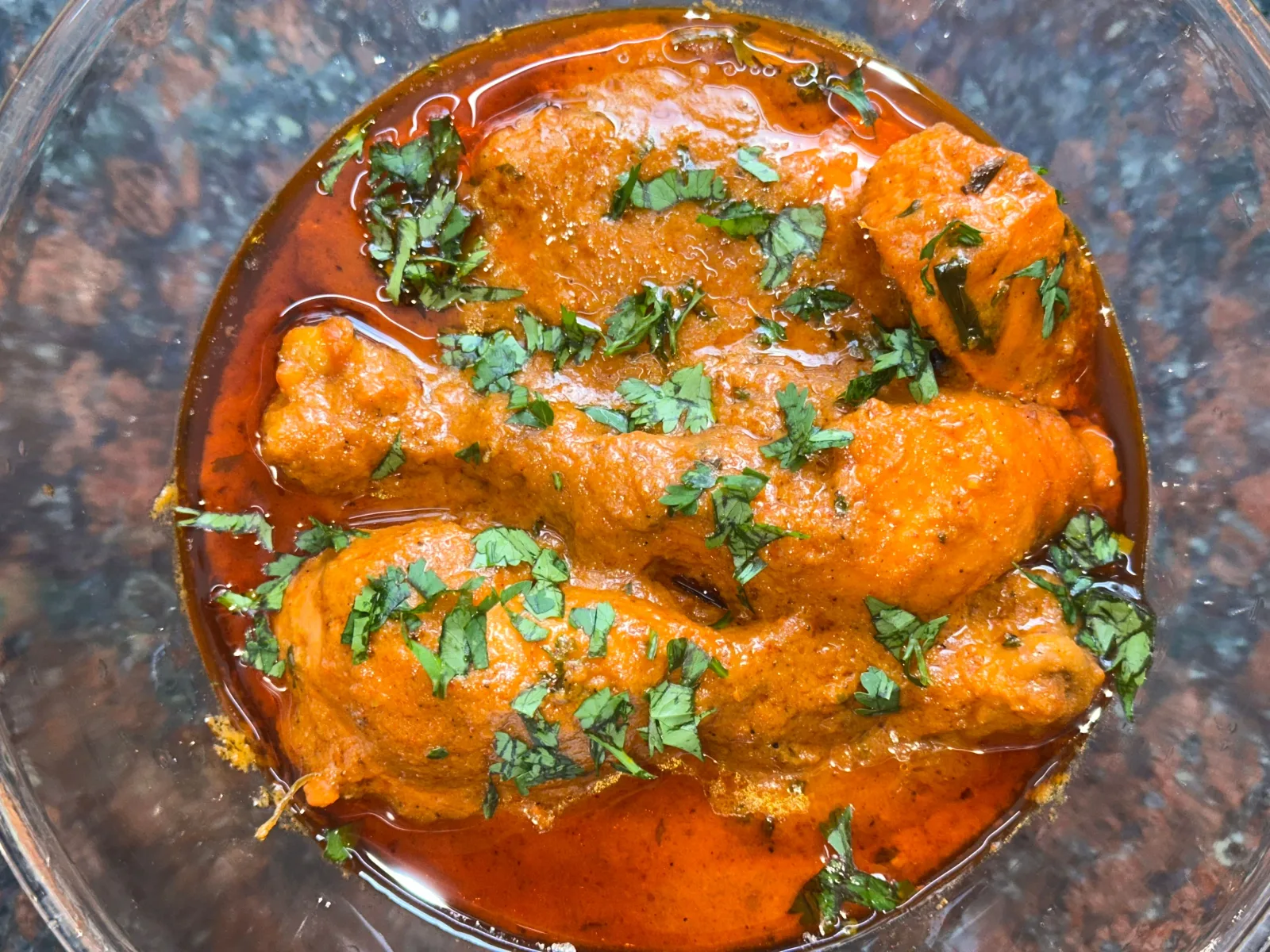 A pot of creamy golden chicken korma garnished with coriander and green chillies, served with naan and basmati rice.