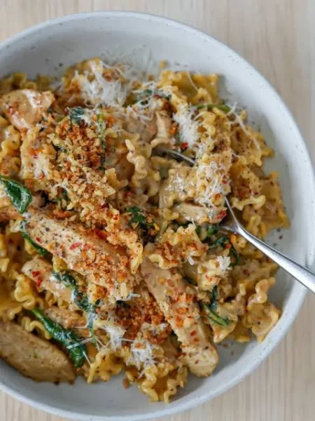 Bowl of spicy chicken macaroni with capsicum, carrot and fresh coriander on a wooden table