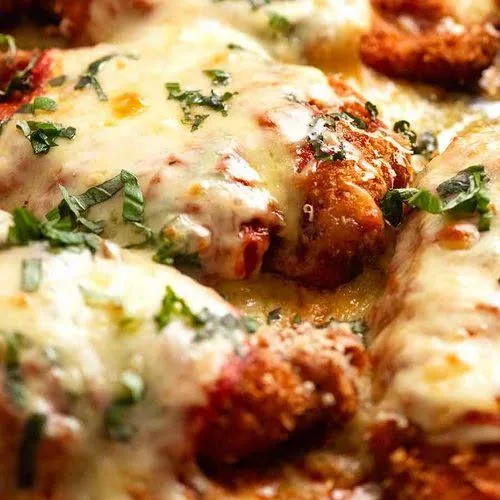 Baked chicken parmesan cutlets with melted mozzarella, tomato sauce and fresh basil in a baking dish