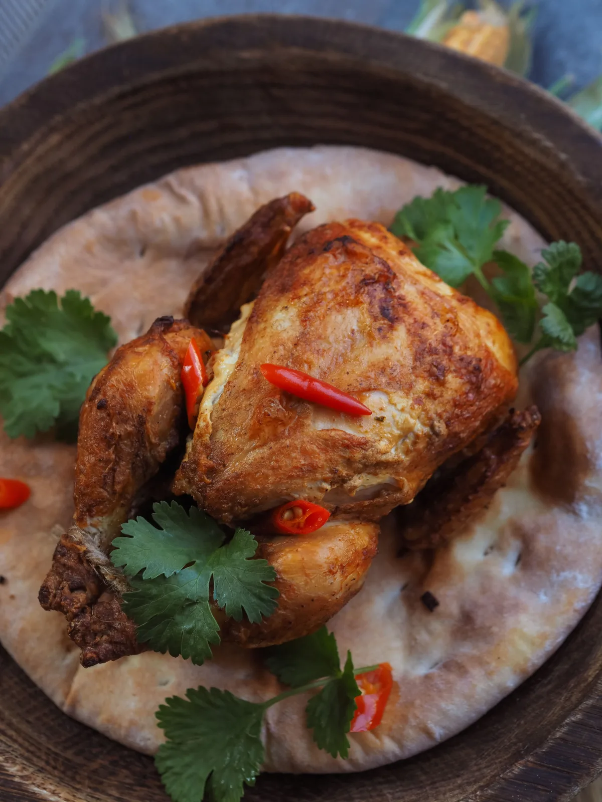 Whole roasted chicken sajji with spiced rice stuffing, roasted potatoes and lemon wedges on a wooden board