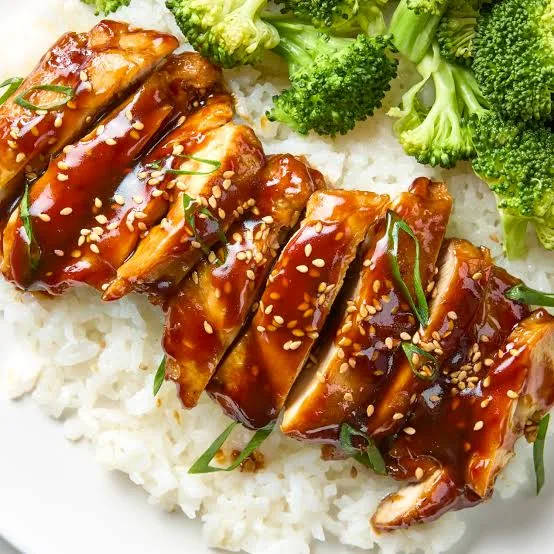 Sliced chicken teriyaki with glossy glaze, rice and broccoli on a white plate