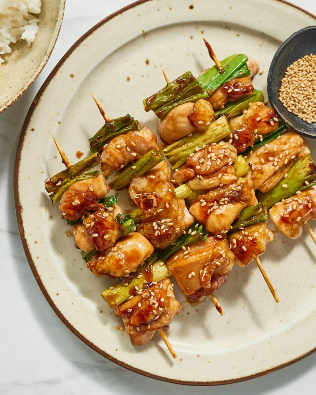 Glazed chicken yakitori skewers with spring onion on a dark plate with lemon wedges and dipping sauce