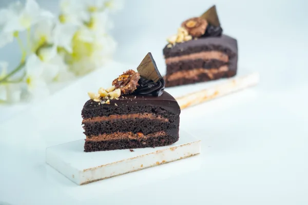 Sliced two-layer chocolate cake with glossy chocolate ganache on a white cake stand