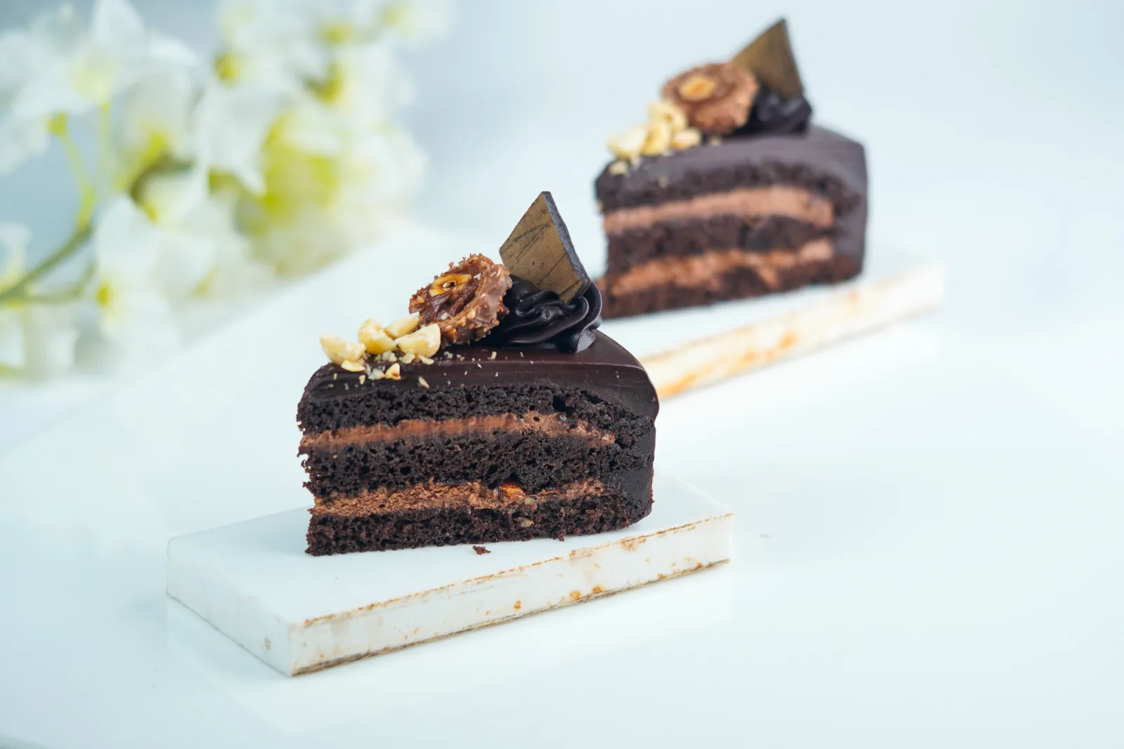 Sliced two-layer chocolate cake with glossy chocolate ganache on a white cake stand
