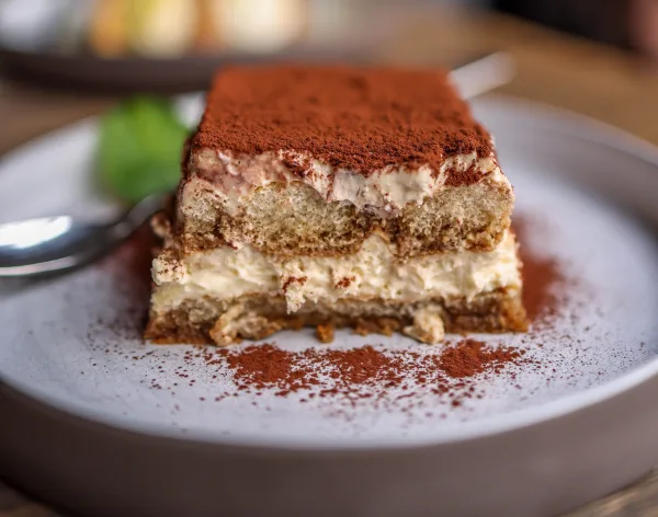 A slice of coffee tiramisu with visible layers of ladyfingers and mascarpone cream, dusted with cocoa powder