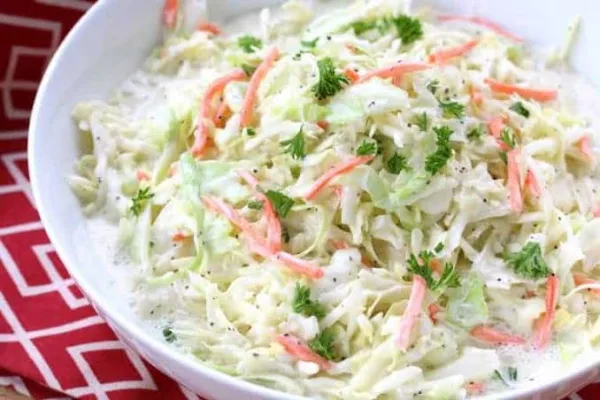 A white bowl of creamy coleslaw with shredded cabbage, carrot and fresh parsley