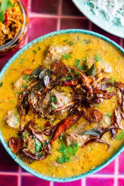 A pot of Pakistani daal gosht with mutton pieces, garnished with coriander, ginger and garlic tarka, served with roti