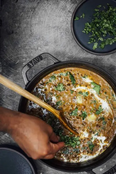 A bowl of creamy dal makhani topped with cream and butter, served with naan and lemon wedges