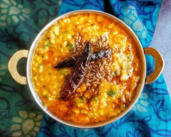 A bowl of golden dal tadka topped with garlic, red chilli and coriander, served with rice and roti