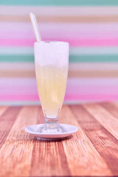 Two tall glasses of pale pink Doodh Soda with ice and a fizzy foam top, garnished with dried rose petals