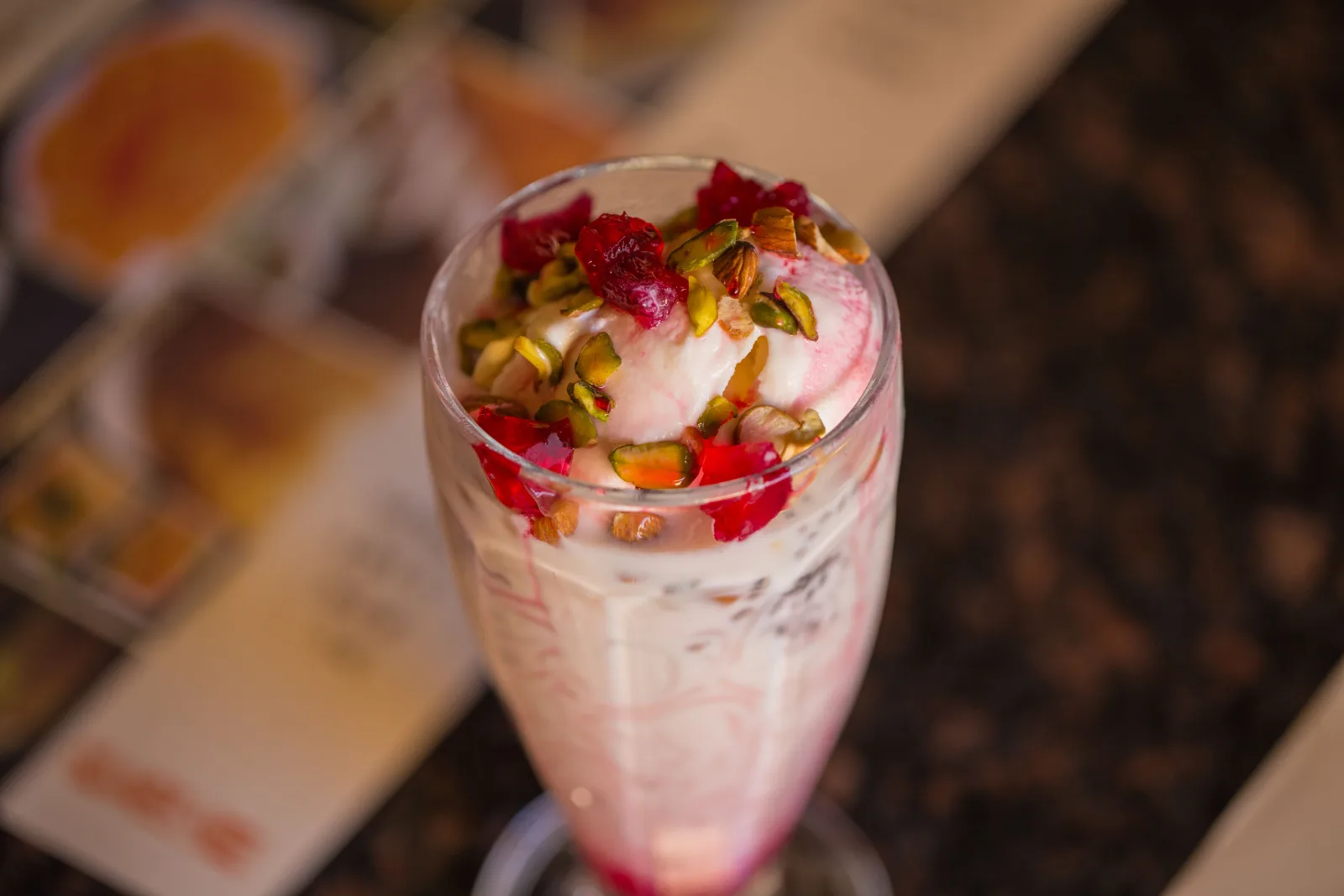 Tall glasses of pink falooda layered with vermicelli, basil seeds and jelly, topped with ice cream and nuts