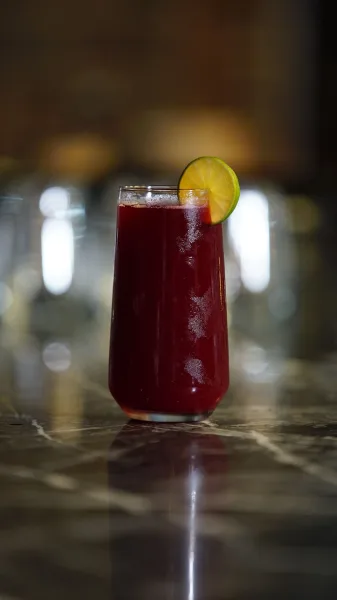 Glasses of deep purple falsa sharbat with ice and mint beside a bowl of fresh falsa berries