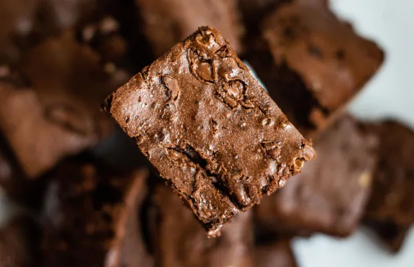 Squares of fudgy chocolate brownies with crackly tops stacked on baking paper, one broken open to show a moist centre