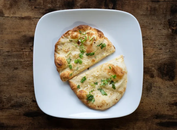 Stack of golden garlic naan brushed with garlic butter and coriander on a wooden board