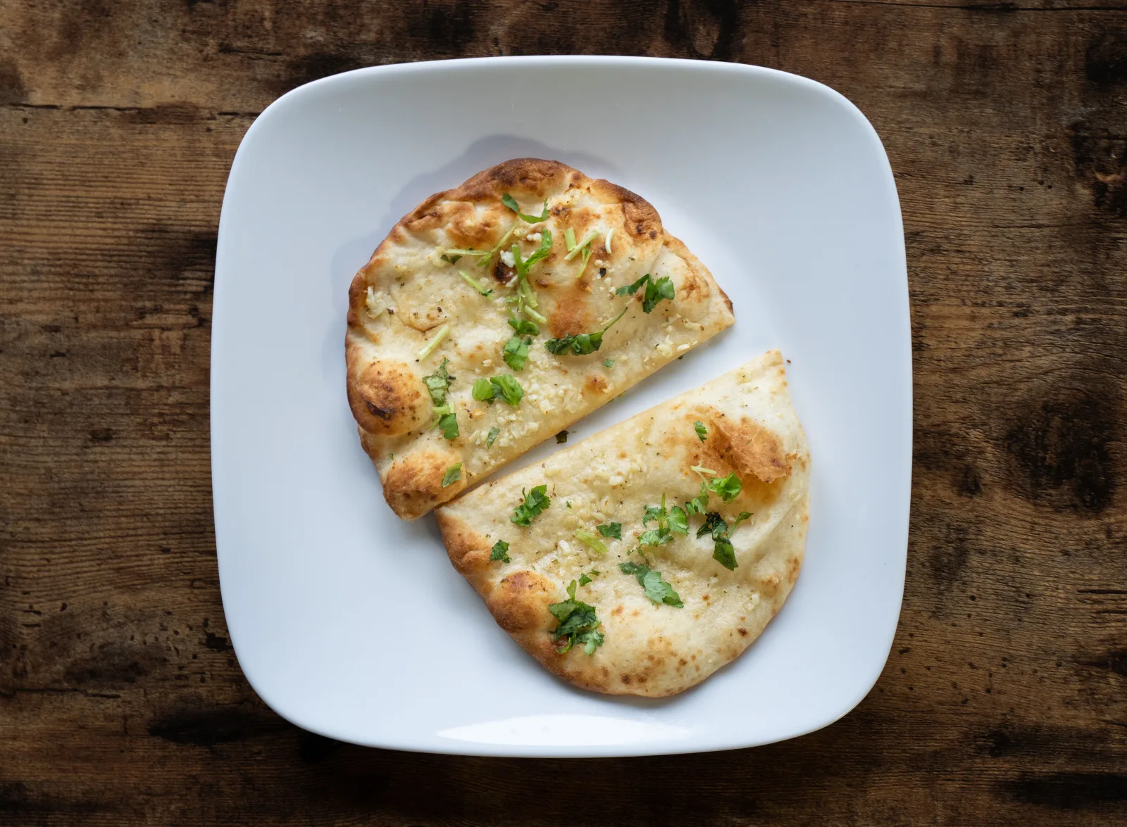 Stack of golden garlic naan brushed with garlic butter and coriander on a wooden board