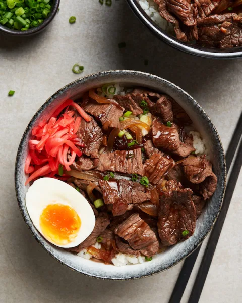 Bowl of gyudon with simmered beef and onions over white rice, topped with spring onions and sesame seeds