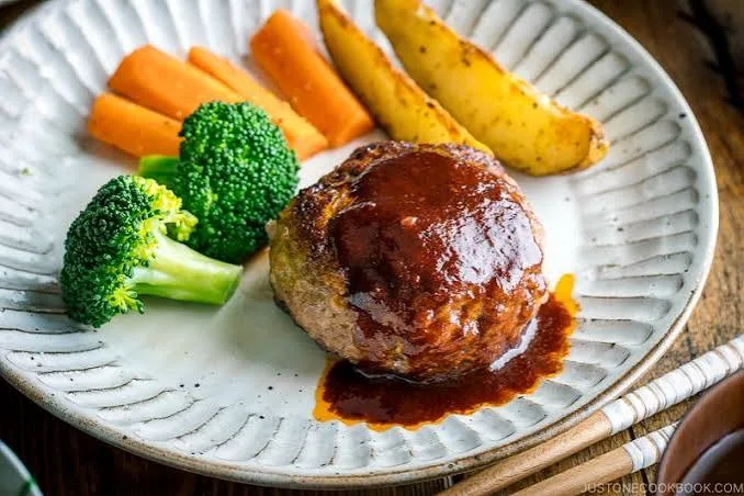 Hambagu steak patties in glossy brown sauce with mushrooms, rice and vegetables on a white plate