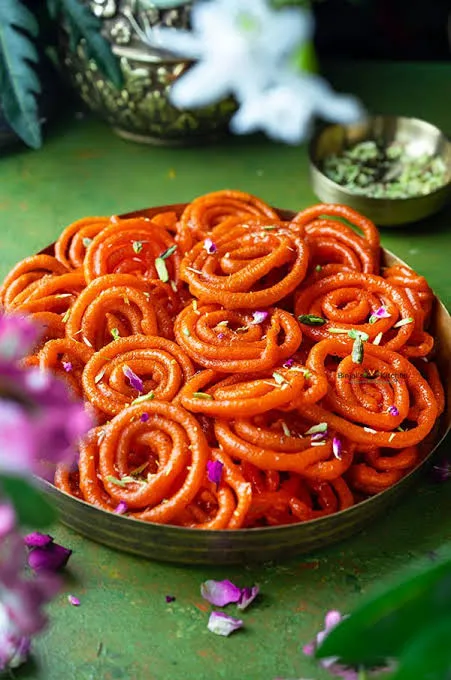 A plate of golden-orange jalebi spirals glistening with saffron syrup and topped with chopped pistachios