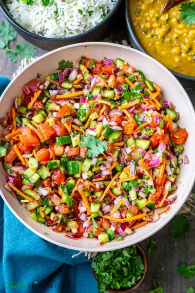 Bowl of diced cucumber, tomato and red onion salad with coriander, mint and pomegranate seeds beside lemon halves