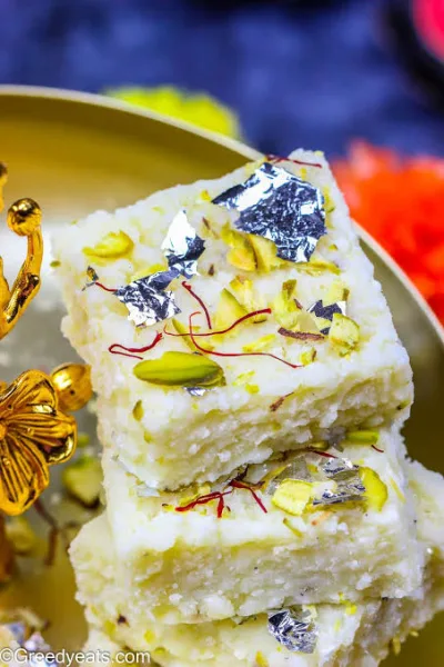 Square pieces of creamy kalakand topped with sliced pistachios on a white plate