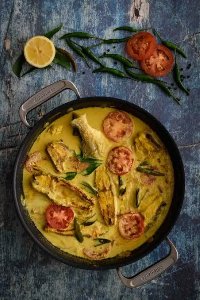 Pan of Kerala fish moilee with white fish pieces in creamy coconut sauce, green chillies and curry leaves