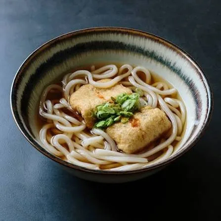 Bowl of kitsune udon with sweet simmered tofu pouches, spring onions and carrot in golden broth