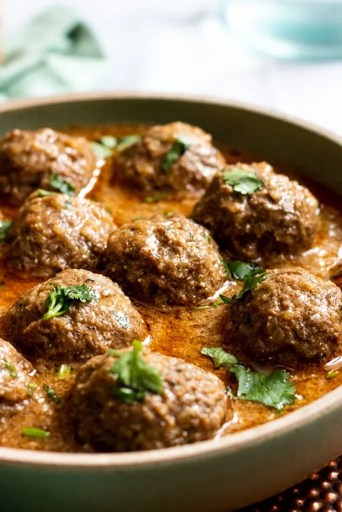 A pot of Pakistani kofta curry with beef meatballs in red tomato gravy, garnished with coriander, ginger and green chillies