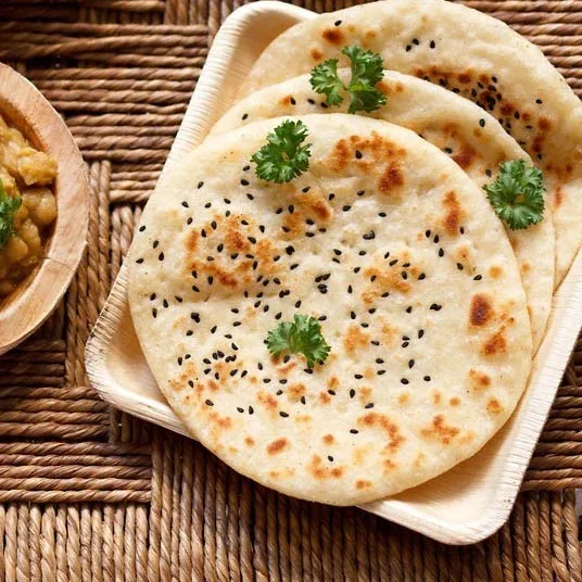 Stack of freshly baked kulcha breads with sesame and nigella seeds on a wooden board