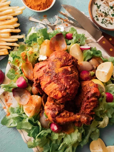 Crispy red-brown Lahori chargha chicken pieces on a steel platter with onions, green chillies, mint and lemon wedges