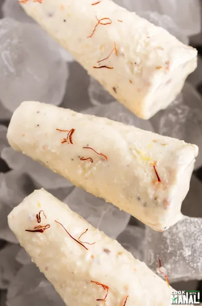 Sliced malai kulfi topped with pistachios and saffron on a copper plate