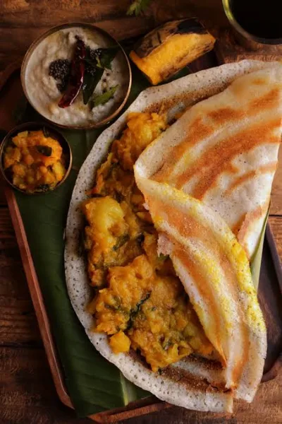 A crisp golden masala dosa filled with spiced potato, served with coconut chutney and sambar on a steel plate