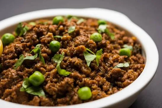 Pot of matar keema with beef mince and green peas, garnished with coriander and ginger, served with roti