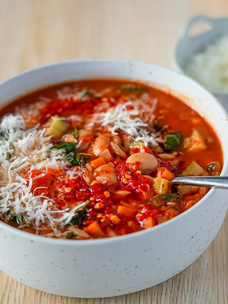 Bowl of chunky minestrone soup with beans, pasta and vegetables topped with Parmesan and basil