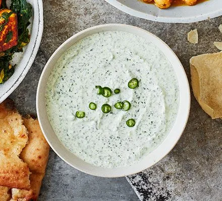 Bowl of creamy pale green mint raita topped with roasted cumin, chilli powder and fresh mint leaves